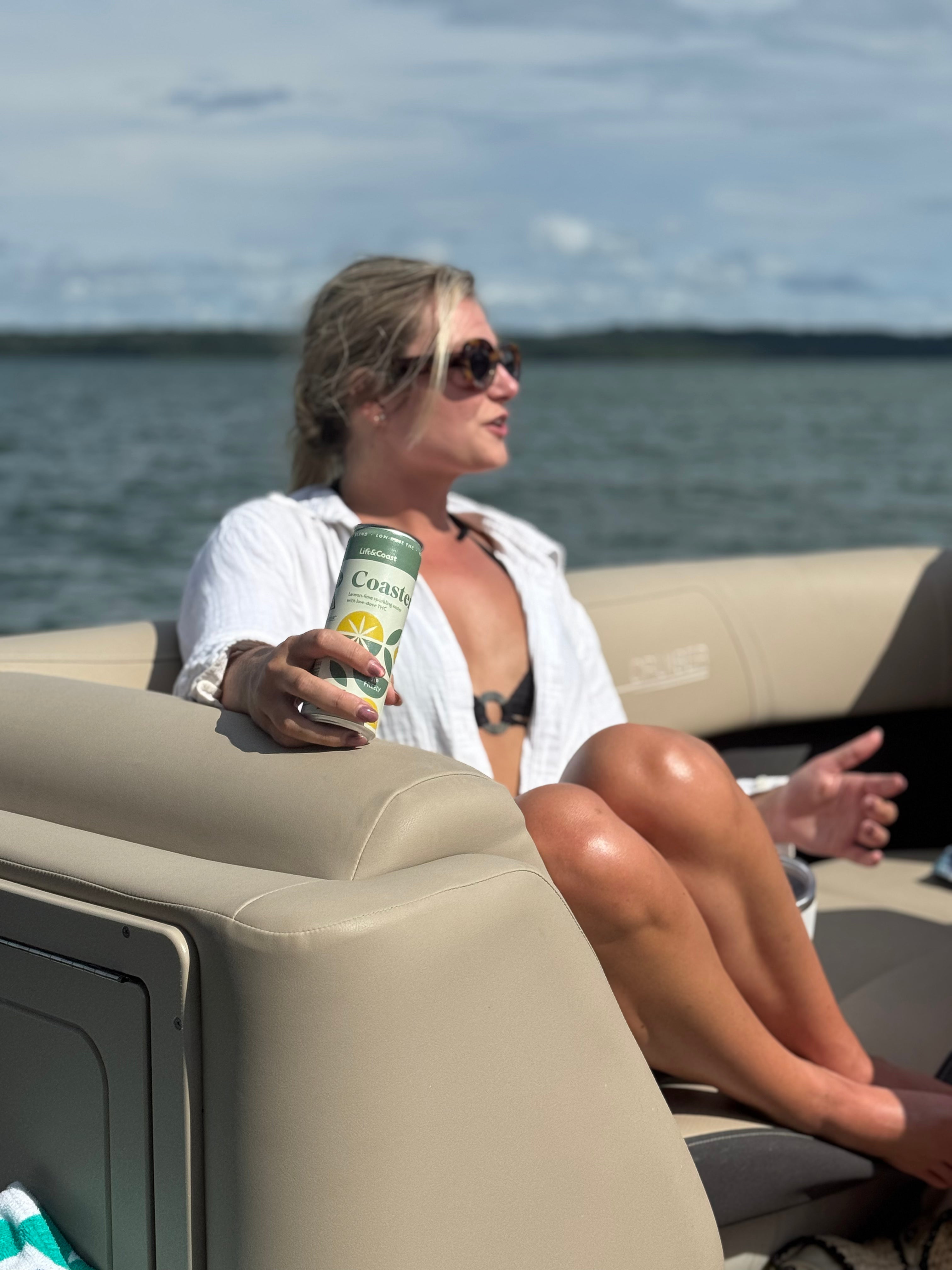 Woman sitting on a boat holding a can of Coaster with water in the background
